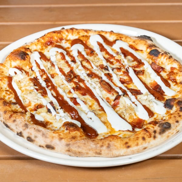 Cali-Forno Pizzeria's BBQ chicken pizza, drizzled with white ranch and red BBQ sauce, on a white plate.