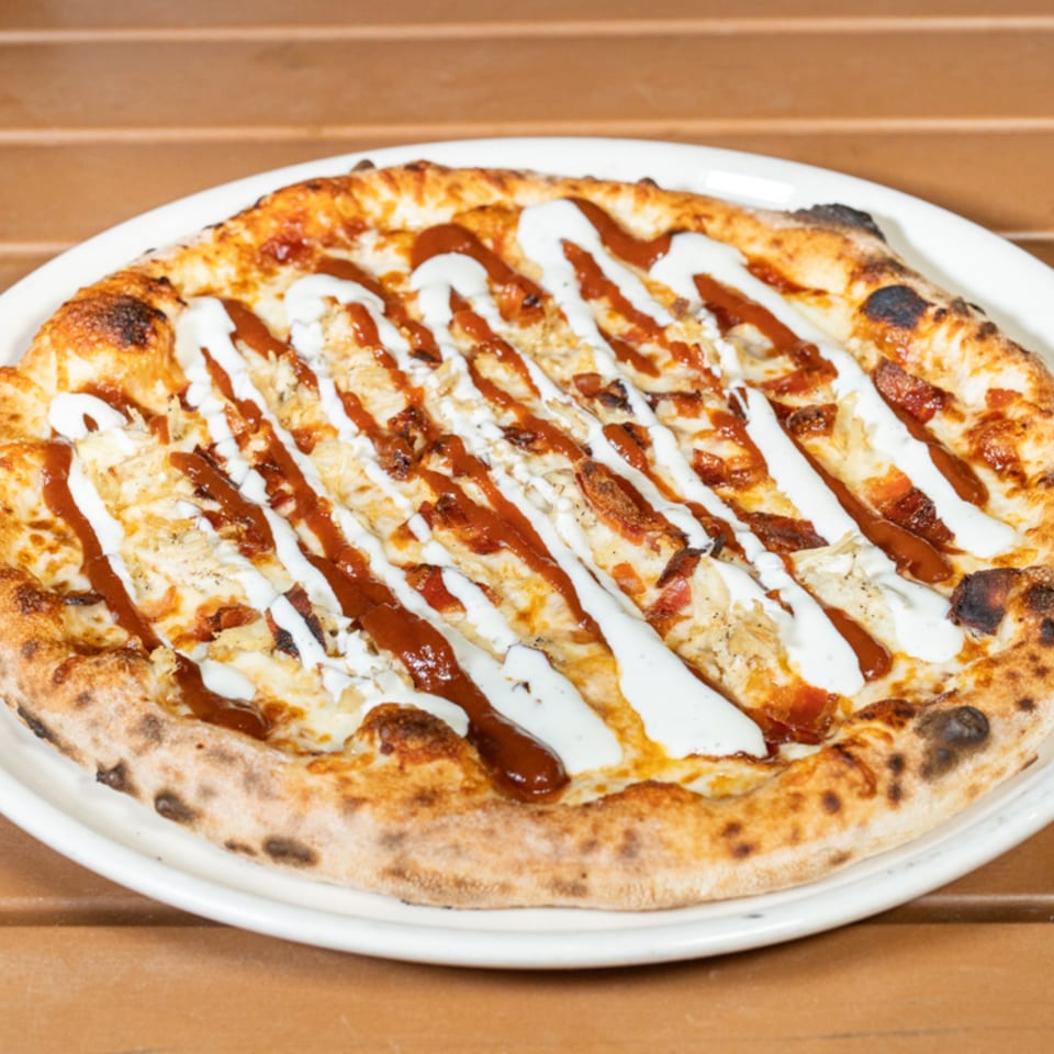 Cali-Forno Pizzeria's BBQ chicken pizza, drizzled with white ranch and red BBQ sauce, on a white plate.