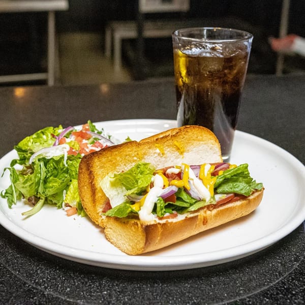 A Cali-Forno Pizzeria sandwich with salad and a drink on a white plate.