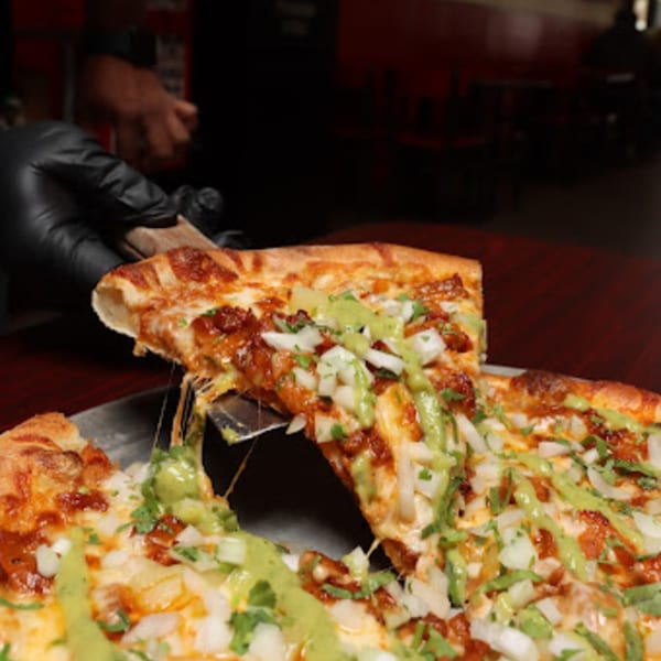 A hand in a black glove lifts a slice of Cali-Forno Pizzeria's pizza with melted cheese and toppings.