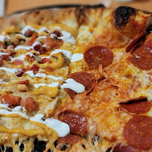 Half pepperoni and half loaded chicken pizza with various sauces and toppings.