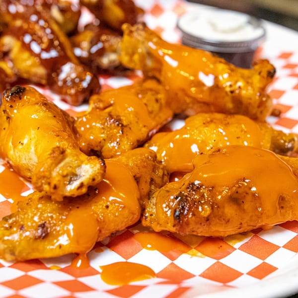 A plate of Cali-Forno Pizzeria's buffalo and BBQ chicken wings with a side of ranch.